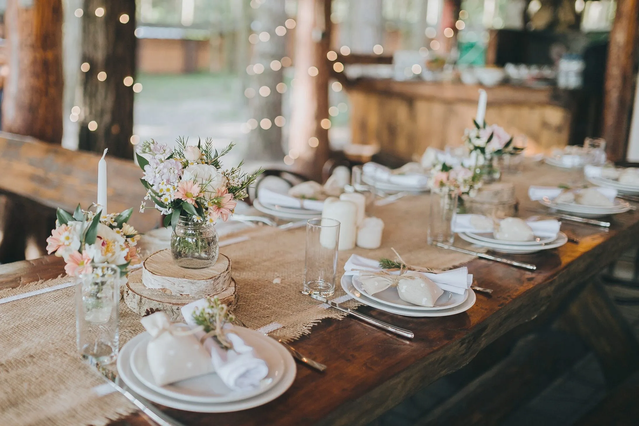 A long wooden table set for a celebration, with flowers, candles and string lights.